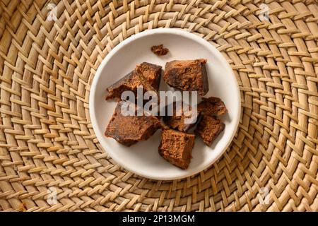 Kithul jaggery et sirop de mélasse sucré naturel de palmier dans un bol blanc sur plateau traditionnel en osier Vue de dessus. Sucre alternatif. Faible niveau de GI alimentaire. Superf Banque D'Images