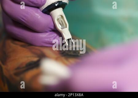 Artiste de l'encre faisant un tatouage avec une machine professionnelle. Gros plan photo du tatouage sur la peau humaine, se concentrer sur les aiguilles Banque D'Images