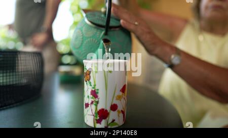 Personne en gros servant du thé dans une tasse. Femme senior tenant la main de la théière en fonte distribuant une boisson chaude à l'extérieur sur la terrasse Banque D'Images