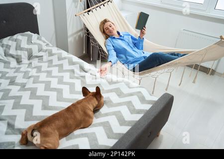 Joyeux femme regardant son chien pendant la lecture Banque D'Images