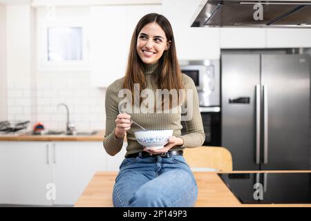 jeune belle femme avec un bol de céréales et une cuillère souriante à la cuisine - la beauté, la nourriture et le concept de femme Banque D'Images