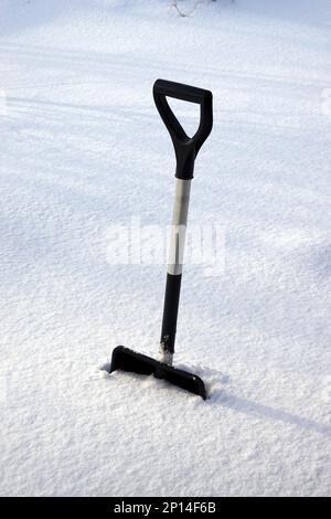 Pelle en métal avec manche noir jaillissée profondément dans la neige sur un terrain de neige lisse Banque D'Images