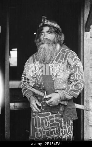 Chef Ainu portant une headaddress et tenant une épée debout dans une porte, 1908. Banque D'Images