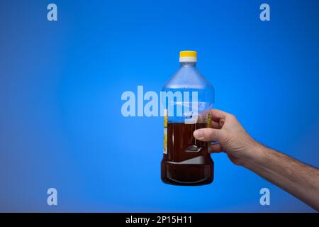 Recyclage de l'huile de cuisson dans une bouteille en plastique transparent. Tenu en main par l'homme. Gros plan en studio, isolé sur fond bleu. Banque D'Images