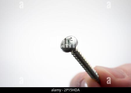 Petite vis filetée en métal maintenue entre les doigts par une main mâle caucasienne. Prise de vue macro en studio, isolée sur fond blanc Banque D'Images