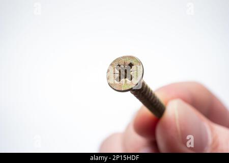 Petite vis filetée en métal maintenue entre les doigts par une main mâle caucasienne. Prise de vue macro en studio, isolée sur fond blanc Banque D'Images