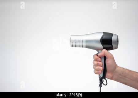 Sèche-cheveux en argent générique tenu en main par le bras mâle caucasien. Gros plan en studio, isolé sur fond blanc. Banque D'Images