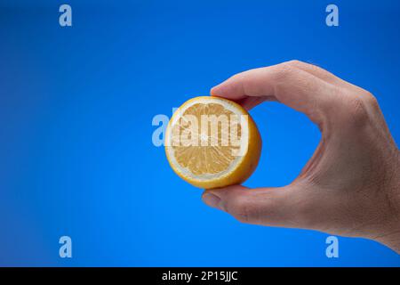Citron mûr frais divisé par deux tenu par la main mâle. Gros plan en studio, isolé sur fond bleu. Banque D'Images