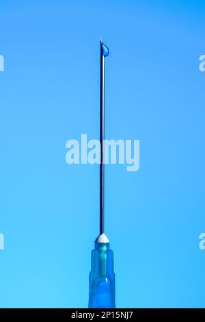 Aiguille de seringue avec goutte de liquide sur l'embout macro isolée sur bleu. Banque D'Images