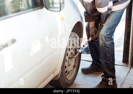 Mécanicien changement d'un pneu de voiture dans un atelier sur une voiture à l'aide d'une perceuse électrique pour desserrer les boulons Banque D'Images