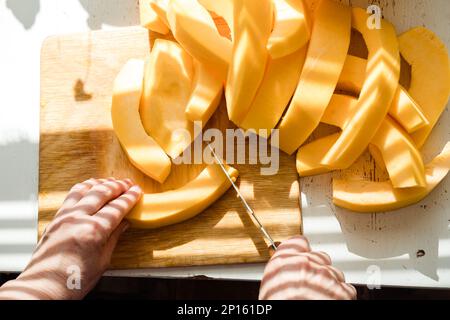 les mains d'une femme avec un couteau coupant une citrouille en morceaux vue du dessus Banque D'Images