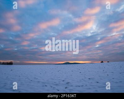 Coucher de soleil spectaculaire et coloré sur un champ de neige blanc avec vue grand angle. Banque D'Images