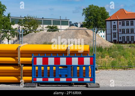Tuyaux en plastique orange et barrière portable le long d'une clôture en treillis métallique. Chantier de construction en arrière-plan. Banque D'Images