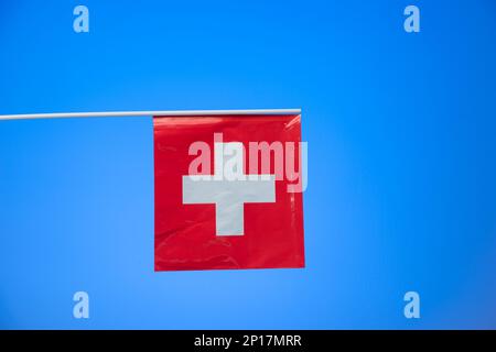 Petit drapeau national suisse isolé sur fond bleu studio tourné. Banque D'Images