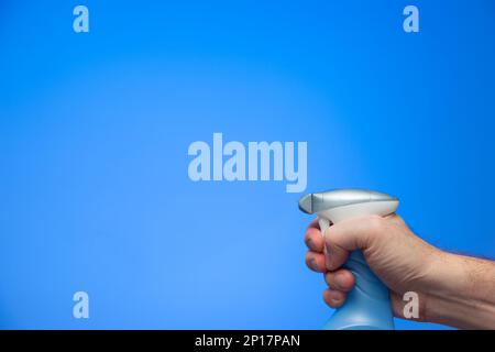 Main mâle caucasienne pinçant une buse de pulvérisation de bouteille en plastique isolée sur fond bleu prise en studio. Banque D'Images