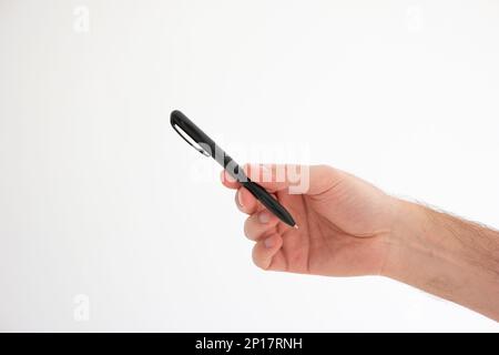 Stylo bille en plastique noir tenu à la main par la main mâle caucasienne faisant geste studio tourné isolé sur blanc. Banque D'Images