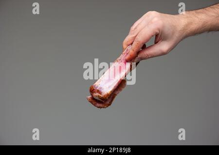 Côte de porc en tranches assaisonnée et crue tenue par un mâle caucasien tiré en studio isolé sur fond gris. Banque D'Images