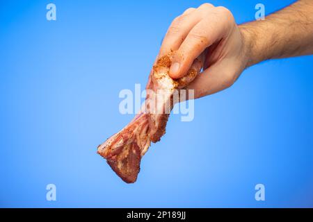 Côte de porc en tranches assaisonnée et crue tenue par un mâle caucasien tiré en studio isolé sur fond bleu. Banque D'Images