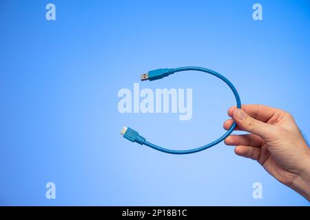 Câble HDMI plié en bleu tenu à la main par un studio de main mâle caucasien tourné isolé sur fond bleu. Banque D'Images
