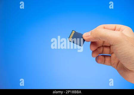 Petite carte mémoire SD en plastique tenue à la main par un studio de main mâle caucasien isolé sur fond bleu. Banque D'Images