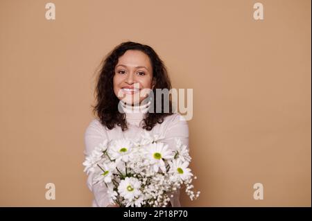 Une femme hispanique stupéfiante ressent le bonheur tandis qu'elle reçoit un joli bouquet de fleurs de chrysanthème pour la Journée internationale de la femme Banque D'Images