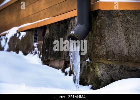 drainpipe de glace près de la fondation en pierre d'une vieille maison en hiver Banque D'Images