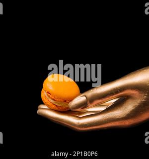 Image rapprochée d'une main humaine tenant un en-cas macaroni orange sur fond d'une statue de couleur or Banque D'Images