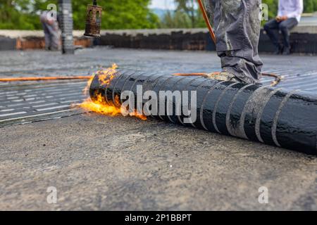 Les travailleurs qui placent un pare-vapeur sur le toit à l'aide d'un chalumeau à gaz propane pour le soudage des feuilles de bitume. Banque D'Images