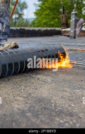 Les travailleurs qui placent un pare-vapeur sur le toit à l'aide d'un chalumeau à gaz propane pour le soudage des feuilles de bitume. Banque D'Images