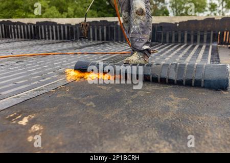 Les travailleurs qui placent un pare-vapeur sur le toit à l'aide d'un chalumeau à gaz propane pour le soudage des feuilles de bitume. Banque D'Images