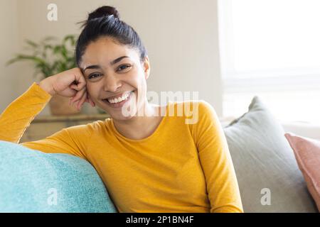 Portrait d'une heureuse femme biraciale assise sur un canapé et souriante Banque D'Images