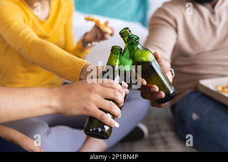 Milieu de divers amis assis sur le sol, manger de la pizza et boire de la bière Banque D'Images
