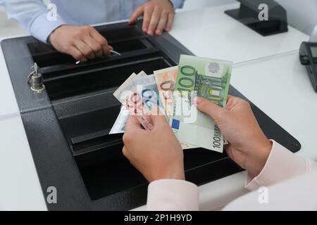 Femme avec de l'argent à la fenêtre du département de devise dans la banque, gros plan Banque D'Images