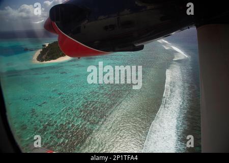 La vue de la fenêtre de l'hydravion sur l'île tropicale et la vague des vagues dans le récif de corail. Voyage romantique, destination de voyage Banque D'Images