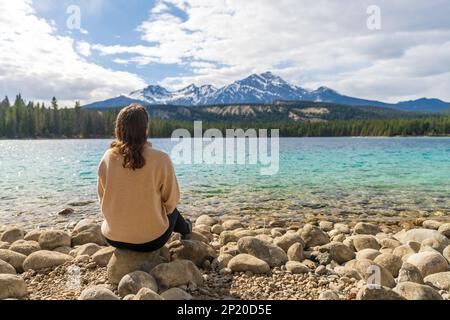 Jeune fille assise au bord du lac et profitant du paysage de la nature. L'été au lac Annette, parc national Jasper, Rocheuses canadiennes, Alberta, Canada Banque D'Images
