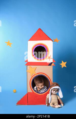 Mignon petit garçon jouant avec une roquette en carton sur fond bleu clair Banque D'Images