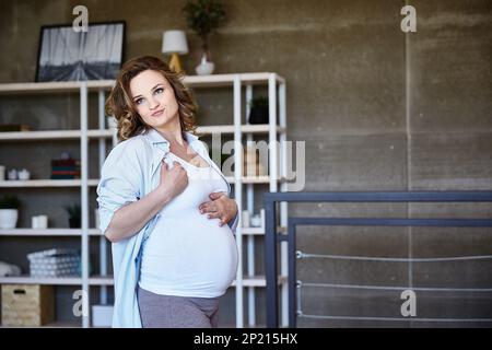 Une charmante fille enceinte regarde son estomac et admire le bébé dans son estomac. Belle fille se sent le bonheur et la bonne santé. Une belle femme Banque D'Images