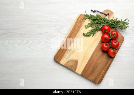 Planche à découper, tomates et romarin sur table en bois blanc, vue de dessus avec espace pour le texte. Ustensile de cuisine Banque D'Images