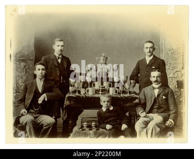 Photo victorienne originale portrait de groupe de gents et d'un enfant. Sur une table, il y a un grand vase de défi de Worcester, / régate trophée pour l'aviron, et d'autres coupes, éventuellement des membres d'une équipe de quatre en boîte. Région de Worcester, Royaume-Uni vers 1897-1899. Banque D'Images