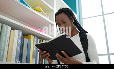 Femme afro-américaine étudiant en train de lire un livre debout dans une salle de classe universitaire Banque D'Images