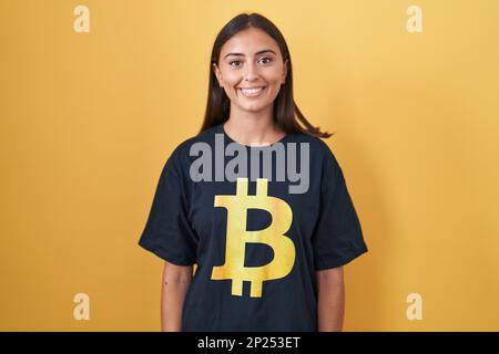 Jeune femme hispanique portant un t-shirt bitcoin avec un sourire heureux et frais sur le visage. personne chanceux. Banque D'Images