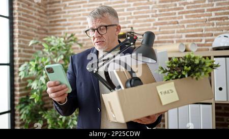 Homme d'affaires d'âge moyen à poil gris licencié en utilisant un smartphone au bureau Banque D'Images