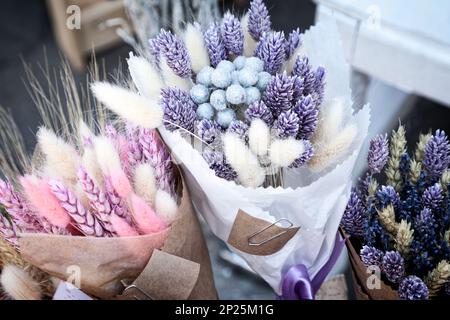 Faites sécher des bouquets colorés de pourpre et de rose aux herbes au fleuriste. De beaux paquets de spikelettes séchées roses et bleues sur un marché - lavande teintée, canari g. Banque D'Images