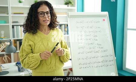 Femme hispanique d'âge moyen enseignant expliquant l'exercice de mathématiques à l'université de bibliothèque Banque D'Images