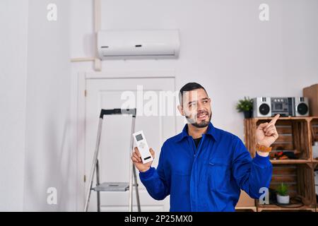 Réparateur hispanique travaillant avec l'air conditionné souriant heureux pointant avec la main et le doigt sur le côté Banque D'Images