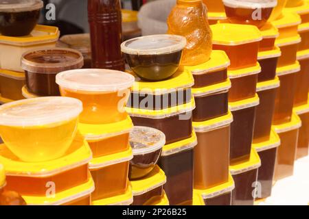 Des piles de conteneurs en plastique avec du miel à un marché alimentaire les agriculteurs. Beaucoup de pots de miel naturel doux de différents types et couleurs à vendre Banque D'Images