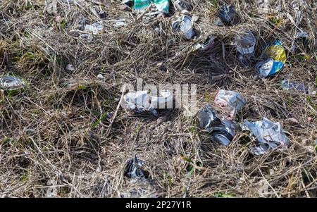 Des boîtes de conserve froissés qui joncissent le sol d'herbe brune morte Banque D'Images