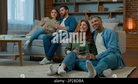 Deux hommes ethniques divers femmes regarder la télévision romantique film tv à la maison la famille se reposer sur le canapé et les amis multiraciaux de plancher regardant le film de comédie Banque D'Images