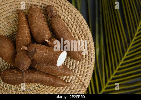 Tubercule de manioc cru biologique sur plateau en osier et feuilles de palmier. Vue de dessus. Copier l'espace. Racine de manioc Yucca. Banque D'Images