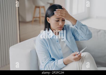 Une femme malsaine souffre de fièvre vérifier la température corporelle, en tenant le thermomètre. Malheureuse jeune femme souffrant de grippe ou de coronavirus mesurant la température Banque D'Images